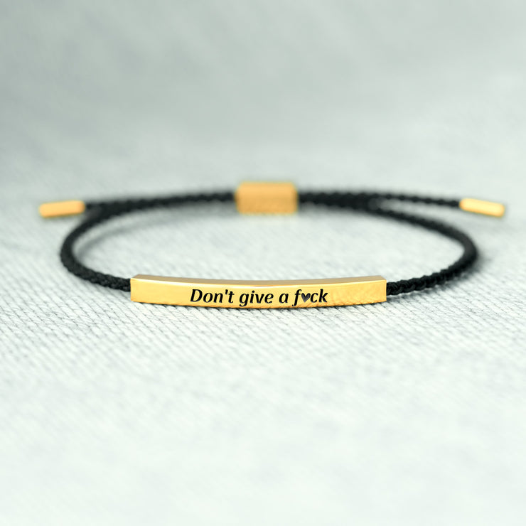 Bracelet with gold bar and black cord on a light gray background